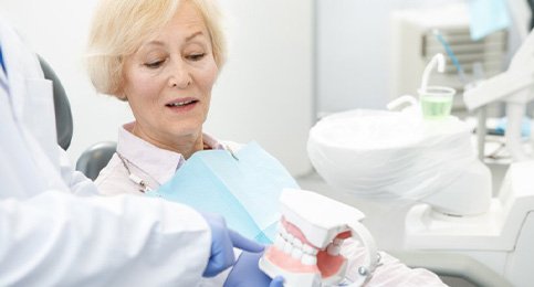 Dentist holding model teeth and discussing dentures with patient